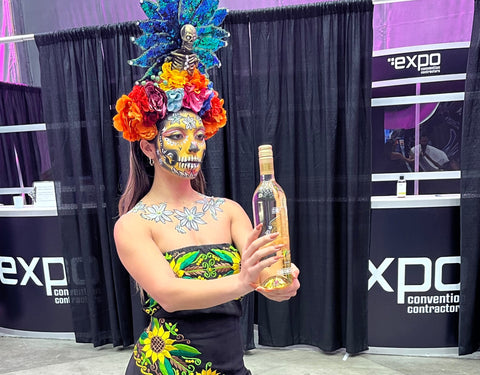 Image of woman in Dia De Los Muertos costume holding bottle of wine